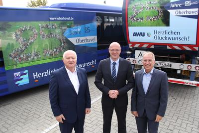 Klaus-Peter Fischer, Ludger Weskamp und Manfred Speder (von links nach rechts) vor Bussen und AWU-Fahrzeugen, die für das Landkreis-Jubiläum werben.
